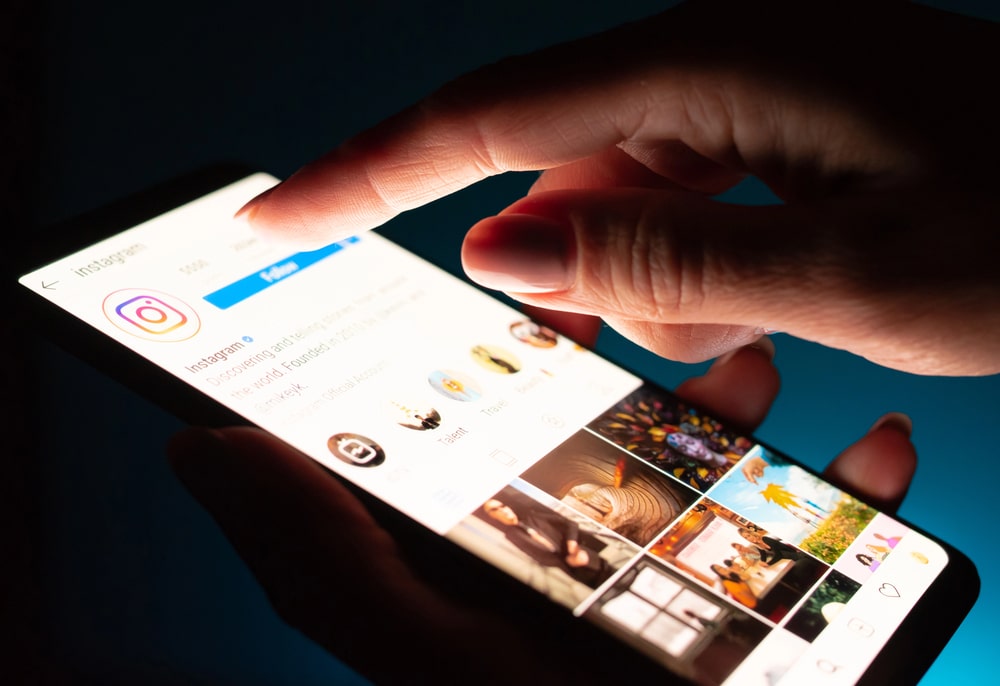 Main de femme utilisant l’application Instagram sur un smartphone dans la pénombre